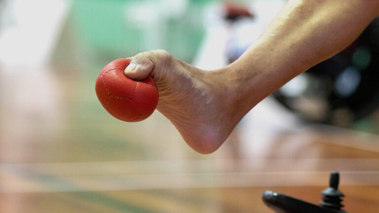 Atleta da Bocha Paralímpica segurando a bola com o pé - Arremesso