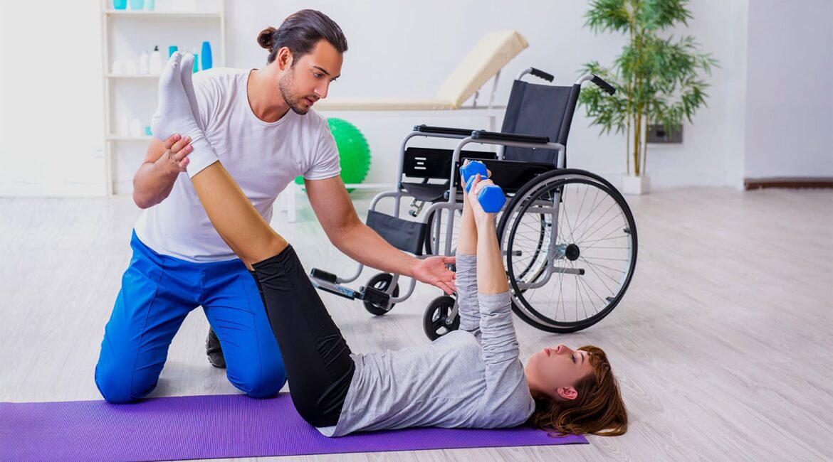 Fisioterapeuta homem atendendo mulher cadeirante, que está deitada realizando exercício, pelo Dia Nacional do Físio e do T.O. 2020