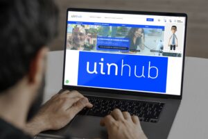Pessoa branca usando laptop aberto na plataforma UinHub. Descrição na legenda.