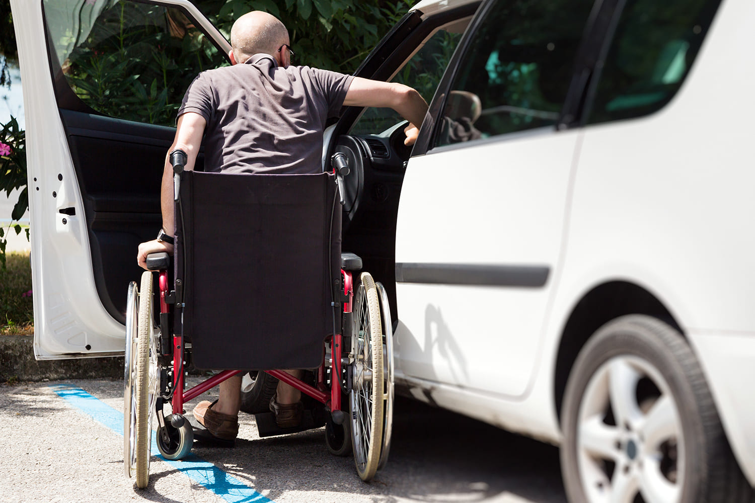 Pessoa calva, em cadeira de rodas, fazendo transferência da cadeira para o carro, ilustra matéria "Versão digital do cartão de estacionamento".