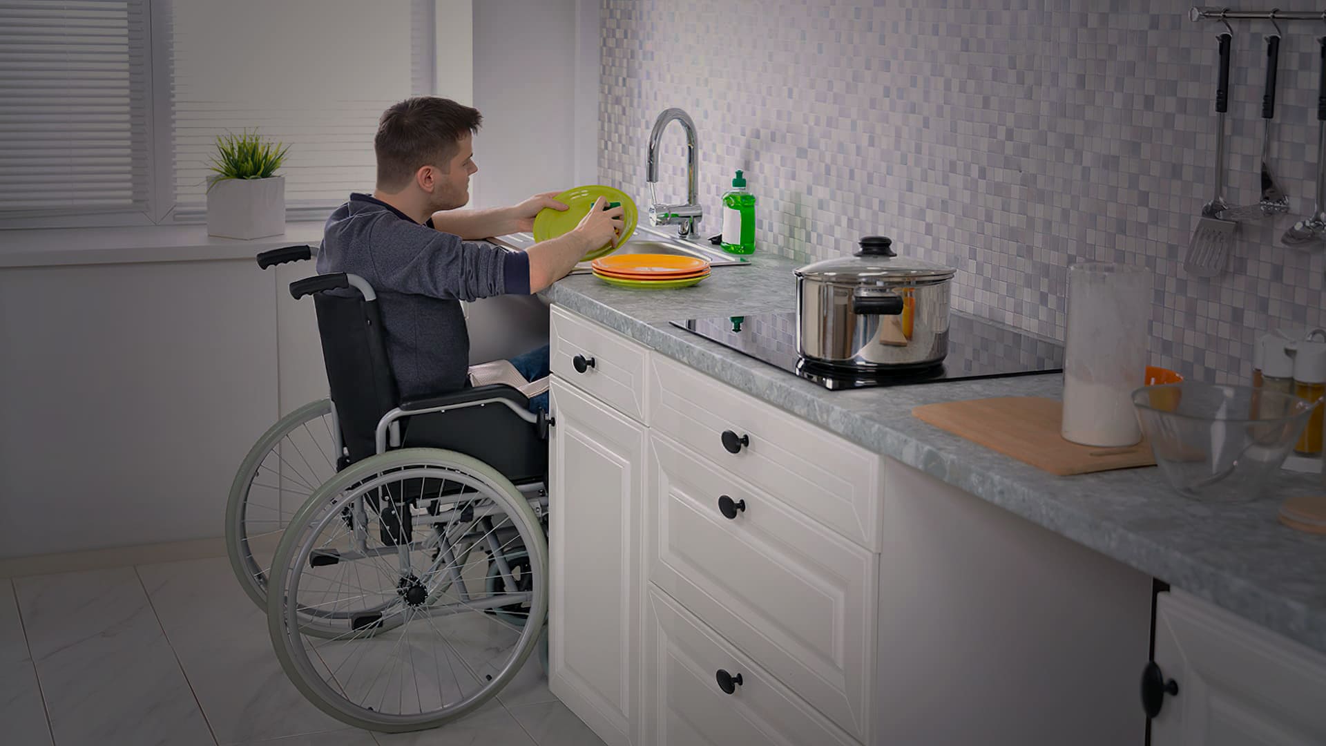 Homem em cadeira de rodas lavando a louça. Descrição na legenda do artigo sobre a importância da acessibilidade em projetos arquitetônicos.