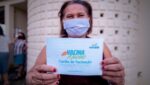 Fotografia da presidente da Associação de Cegos de Alagoas, Cícera Oliveira da Cruz segurando o cartão de vacinação da COVID-19 em braille.