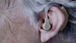 Fotografia de orelha com aparelho auditivo, ilustrando o texto "Pessoas surdas podem denunciar em Libras violações de Direitos Humanos no BR".