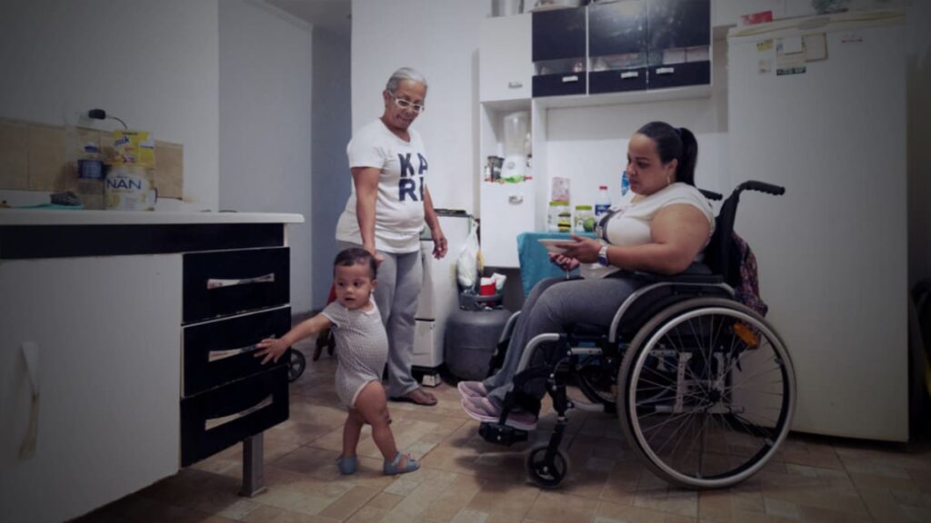 A venezuelana Gabriela Peña, mulher em cadeira de rodas, em frente da filha de 1 anoi, segurando a mão da avó.
