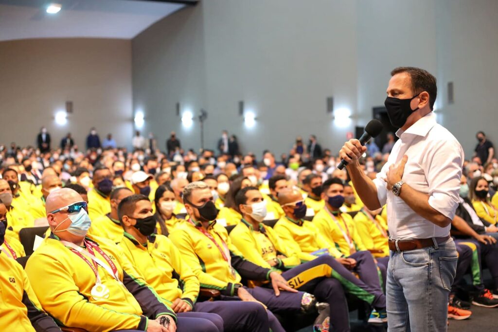 Programa Cidade Acessível: Governo de SP promete cidades mais inclusivas e acessíveis 2 Foto do Governador de SP, em frente aos atletas paralímpicos, usando uniforme do Brasil, durante homenagem.