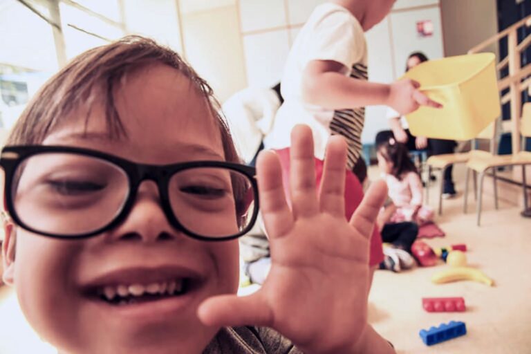 Criança usando óculos de grau, interage com fotógrafo, para ilustrar 10 sinais de alerta para detectar o TEA.
