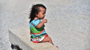 Criança com nanismo sentada em banco de pedra, ilustrando Acondroplasia no desenvolvimento infantil.