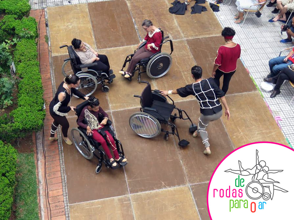 Foto colorida tirada do alto, mostra pessoas em cadeiras de rodas e em pé, dançando.
