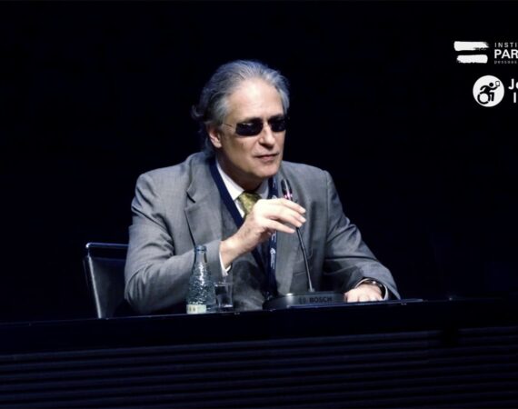 Desembargador cego, Ricardo Tadeu Marques da Fonseca, homem branco de cabelos grisalhos, terno e gravata, e óculos escuros. Discursando no microfone.
