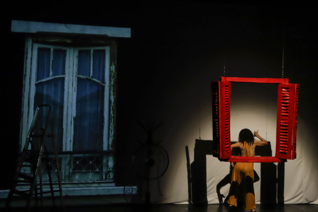 Foto de espetáculo com artista de costas e uma janela.