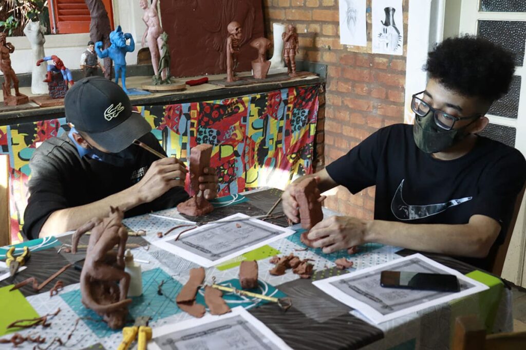 Dois jovens criando mini-esculturas em oficina de artesanato.