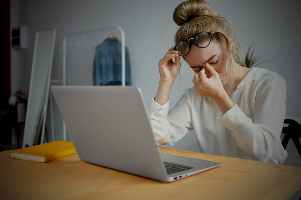 Jovem mulher em frente ao computador, expressando desconforto ou dor de cabeça.