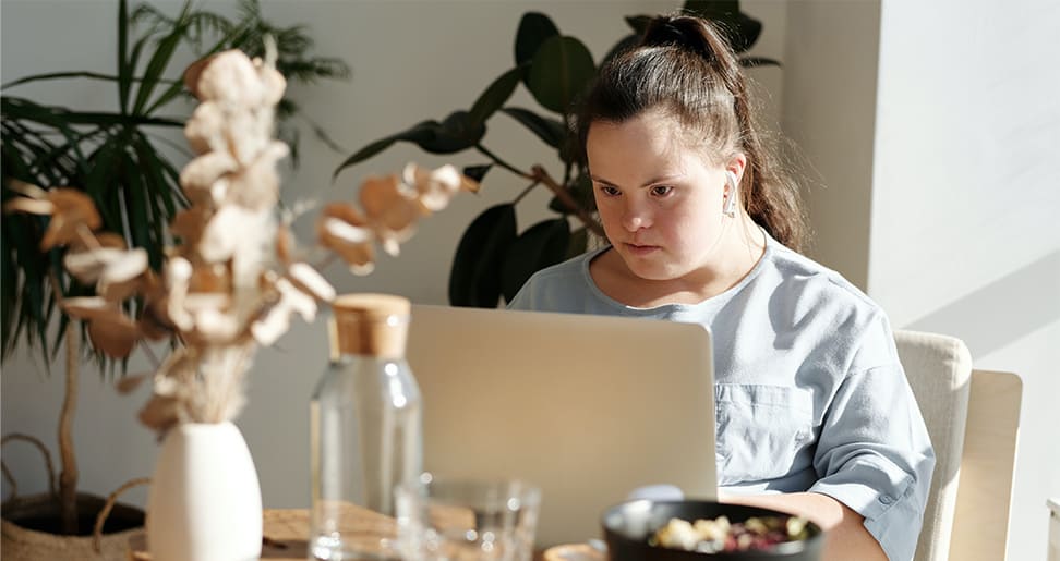 Jovem mulher com T21 utilizando o computador, como ilustração para "bolsa de pós-doutorado sobre síndrome de Down, pela MIT.