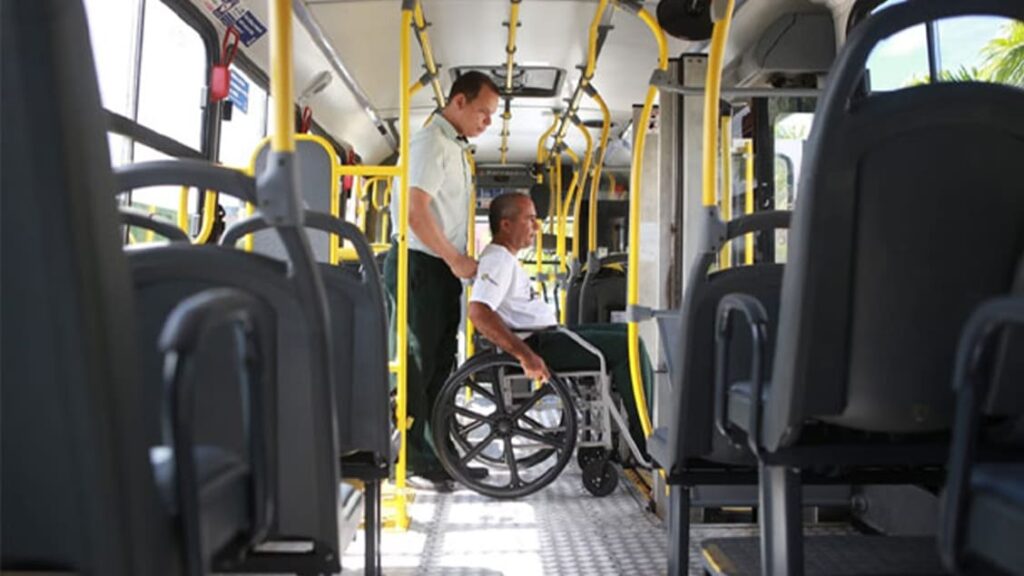 Funcionário do transporte público auxiliando um cadeirante dentro do ônibus.