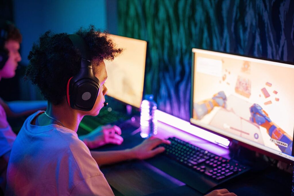 Jovem sentado em frente a tela do computador, jogando videogame, ilustrando a doença "distúrbio em jogos eletrônicos".