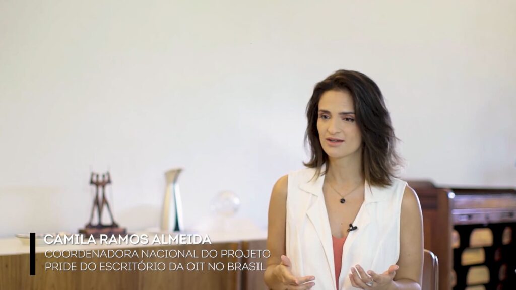 Camila Almeida, coordenadora do Projeto Pride na OIT no Brasil. Ela é uma mulher de pele clara e cabelos escuros na altura dos ombros.
