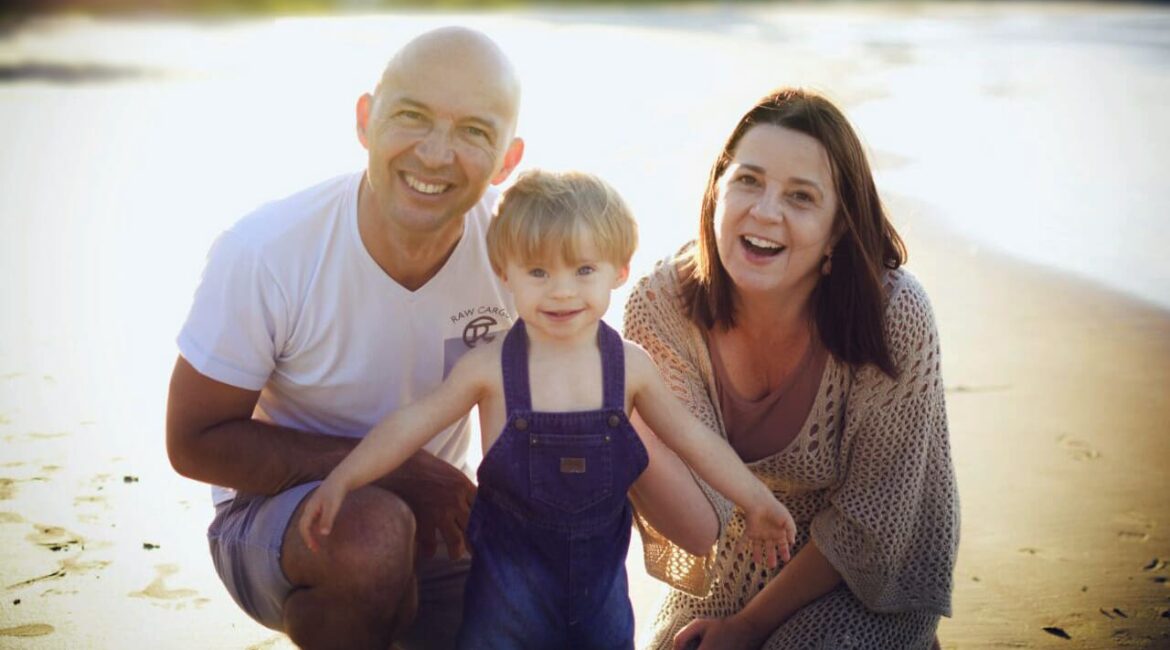 Foto em família com pai, mãe e menino com trissomia do cromossomo 21, notícia “Medicamento para Alzheimer pode melhorar cognição de pessoas com T21.