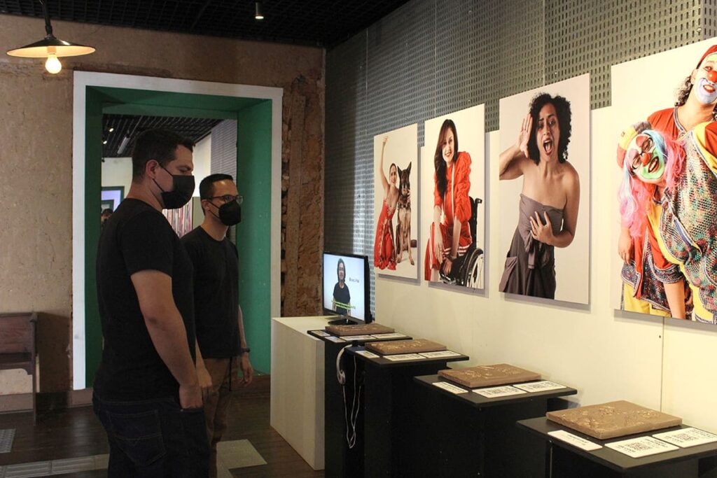 Duas pessoas estão apreciando a exposição "O Ato fotográfico acessível, subversivo e sua transversalidade cultural", no Museu da Energia em Itu (SP).