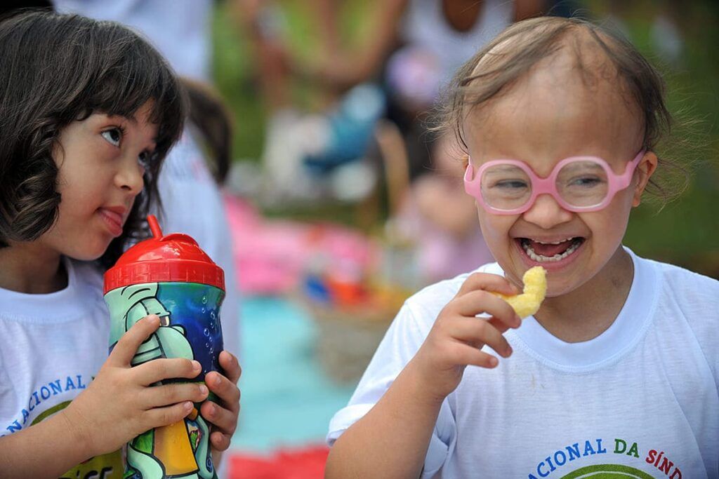 Duas garotinhas com trissomia 21, uma delas usando óculos de grau.
