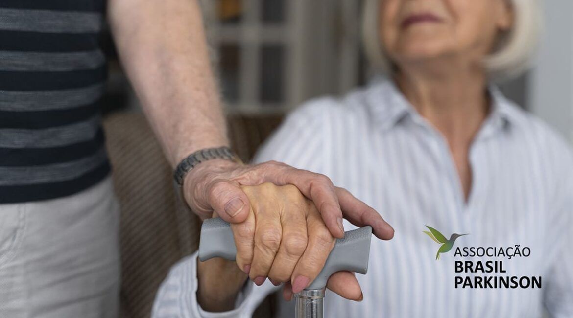 Duas pessoas idosas. Uma segura a mesma bengala e outra segura sua mão. Não se vê seus rostos. ‘Falta de remédios para Parkinson na rede pública de saúde.’