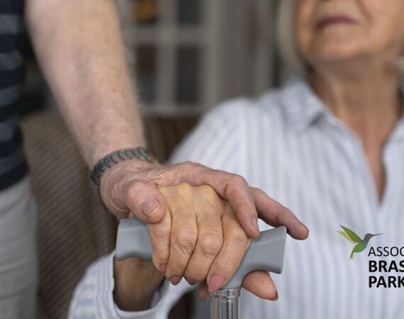 Duas pessoas idosas. Uma segura a mesma bengala e outra segura sua mão. Não se vê seus rostos. ‘Falta de remédios para Parkinson na rede pública de saúde.’