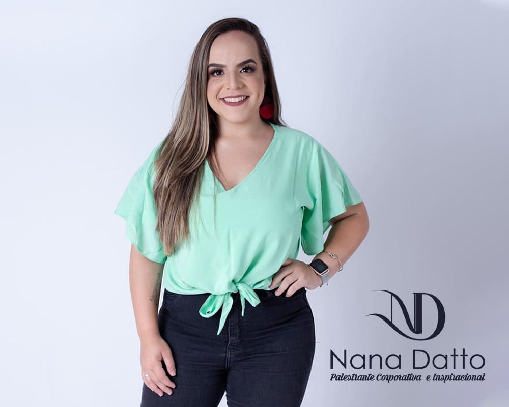 Nana Datto tem pele branca e cabelos longos em tons loiros e castanho claro. Usa camiseta verde clara e calça jeans azul escura.