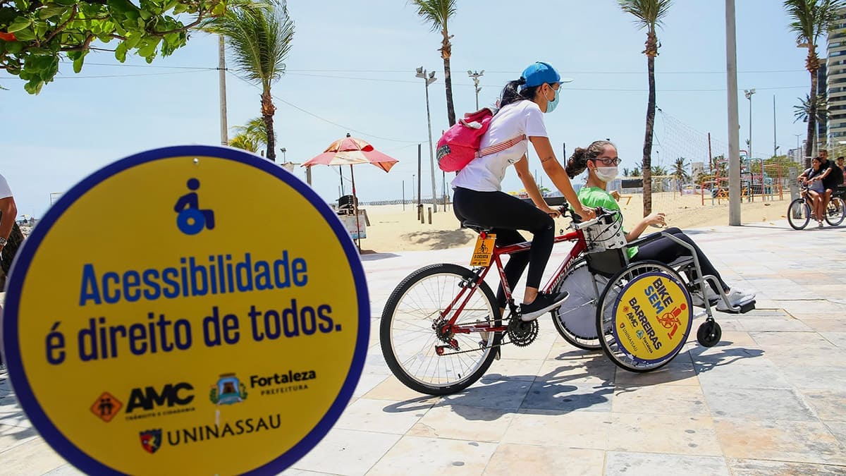 Foto do Bike Sem Barreiras, projeto de bike adaptada para PcDs, com duas pessoas: Uma em cima da bicicleta e outra na cadeira de rodas, que serve como roda frontal da bike.