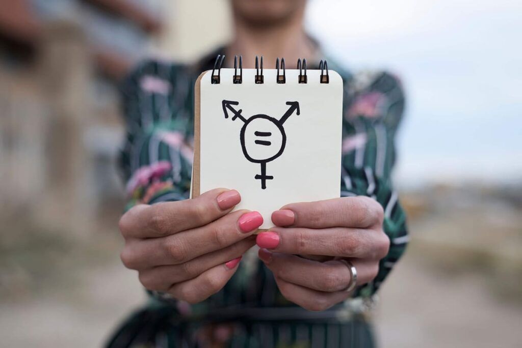 Pessoa mostra caderno com desenho da simbologia da diversidade dos gêneros masculino, feminino e a fusão deles, como transgênero.
