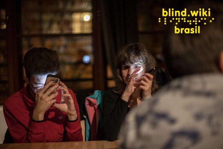 Duas pessoas com deficiência visual utilizando celular. No canto direito superior, sobreposição da logo “BlindWiki Brasil”, grafado em português e em Braille.