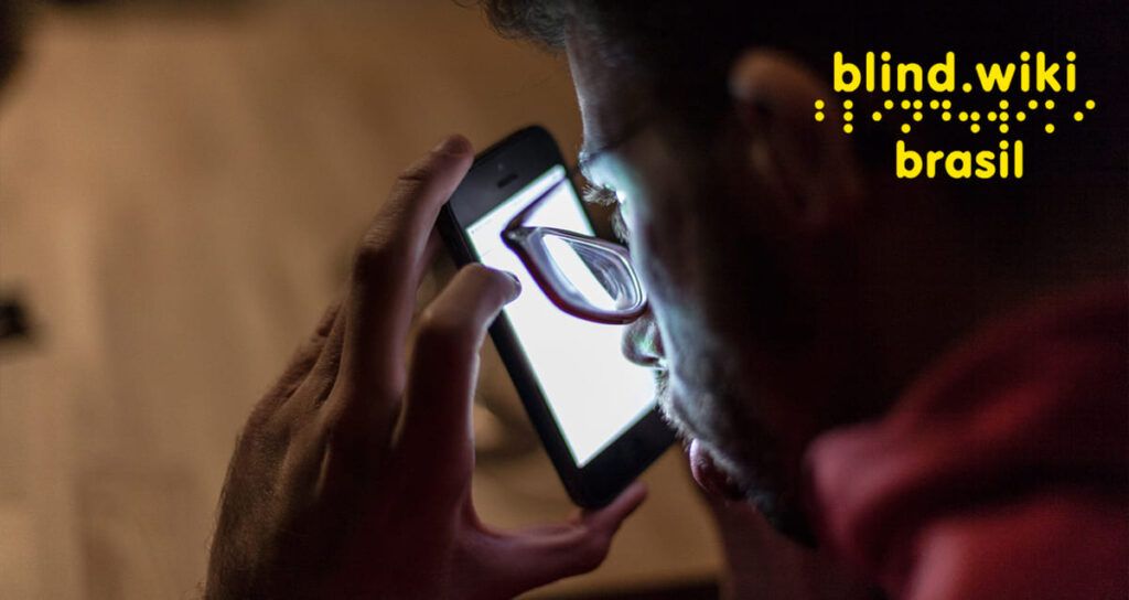 Homem com baixa visão usa óculos de grau e olha para o celular bem próximo ao rosto. No canto direito superior, a logo da BlindWiki Brasil.