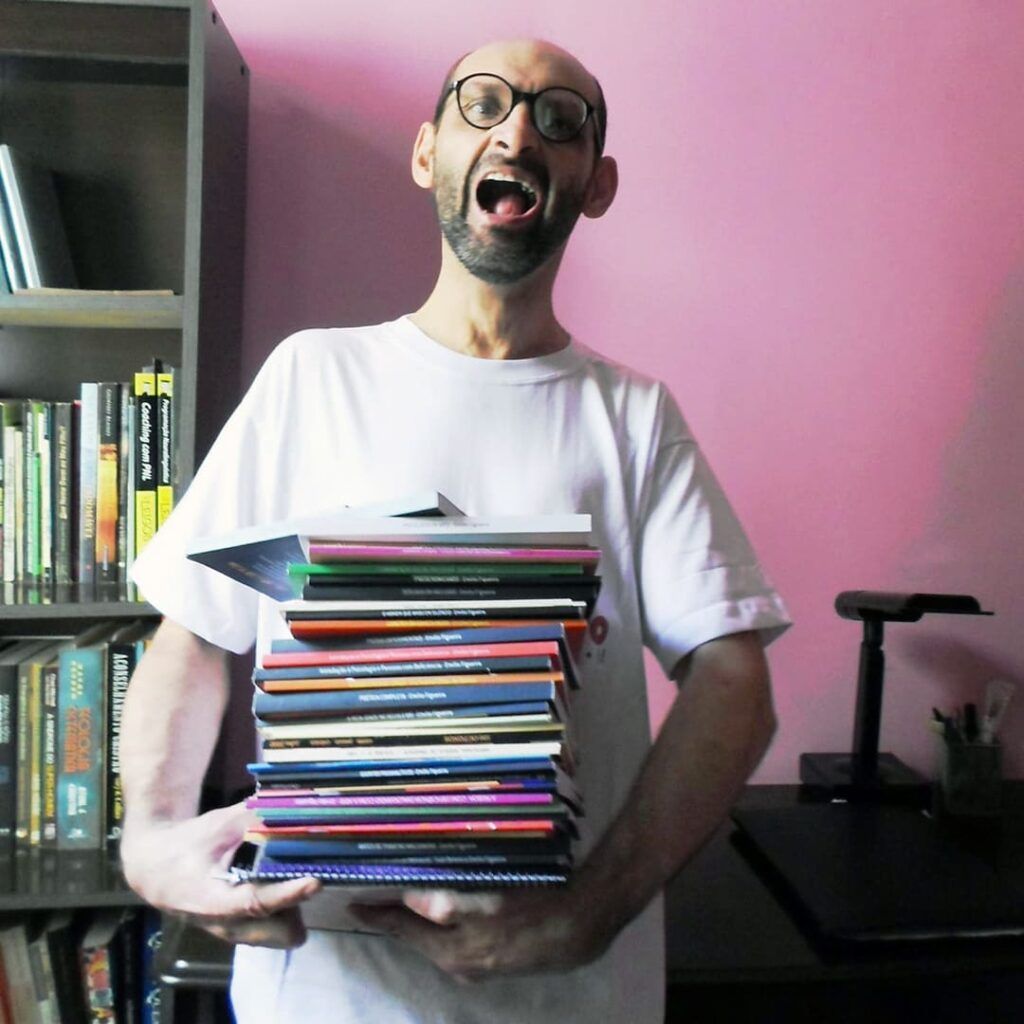 Emilio Figueira está carregando uma porção de livros e sorrindo.