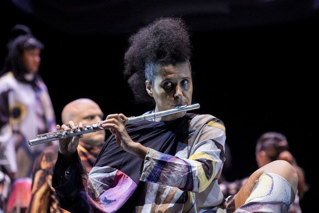 Foto de musicista tocando flauta no palco do musical acessível Museu Nacional - Todas As Vozes Do Fogo.