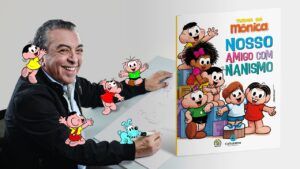 Mauricio de Souza, sentado, desenhando e sorrindo com personagens e capa do livro do personagem com nanismo que estreia na Turma da Mônica.