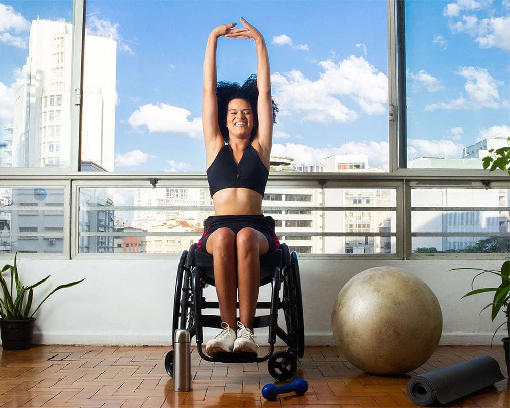 Foto colorida, em ambiente interno, com mulher negra cadeirante praticando atividade física. UinStock: Banco de imagens brasileiro.
