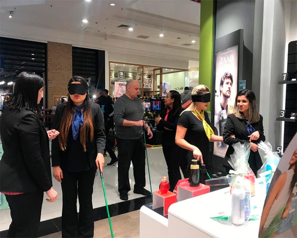 Foto de funcionárias de loja treinada pela startup Inclue, com atendentes usando vendas nos olhos e bengalas para pessoas com deficiência visual