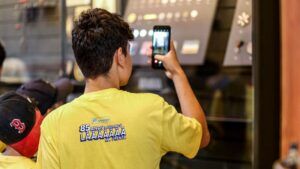 Estudante com camiseta amarela fotografando com o celular. Ipiranga realiza visitação inclusiva com estudantes no Museu.