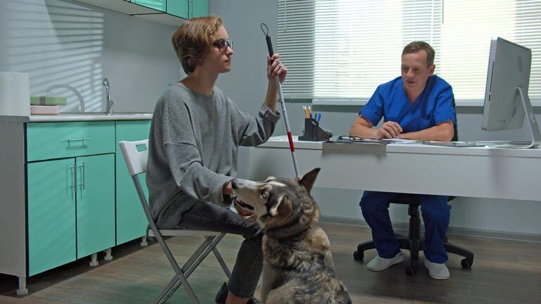 Pessoa cega está sentada em consulta médica, com bengala e cão-guia. Curso de Orientação e Mobilidade em SP.