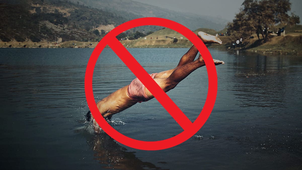 Imagem de pessoa do sexo masculino mergulha de ponta em lago. Sobreposição do símbolo vermelho de proibido sinaliza risco de lesão medular por mergulho.