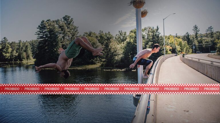 Dois homens saltam em lago, de costas, do alto de uma ponte. Sobreposição digital de faixa vermelha com a palavra “Proibido”, pelo risco de lesão medular por mergulho.