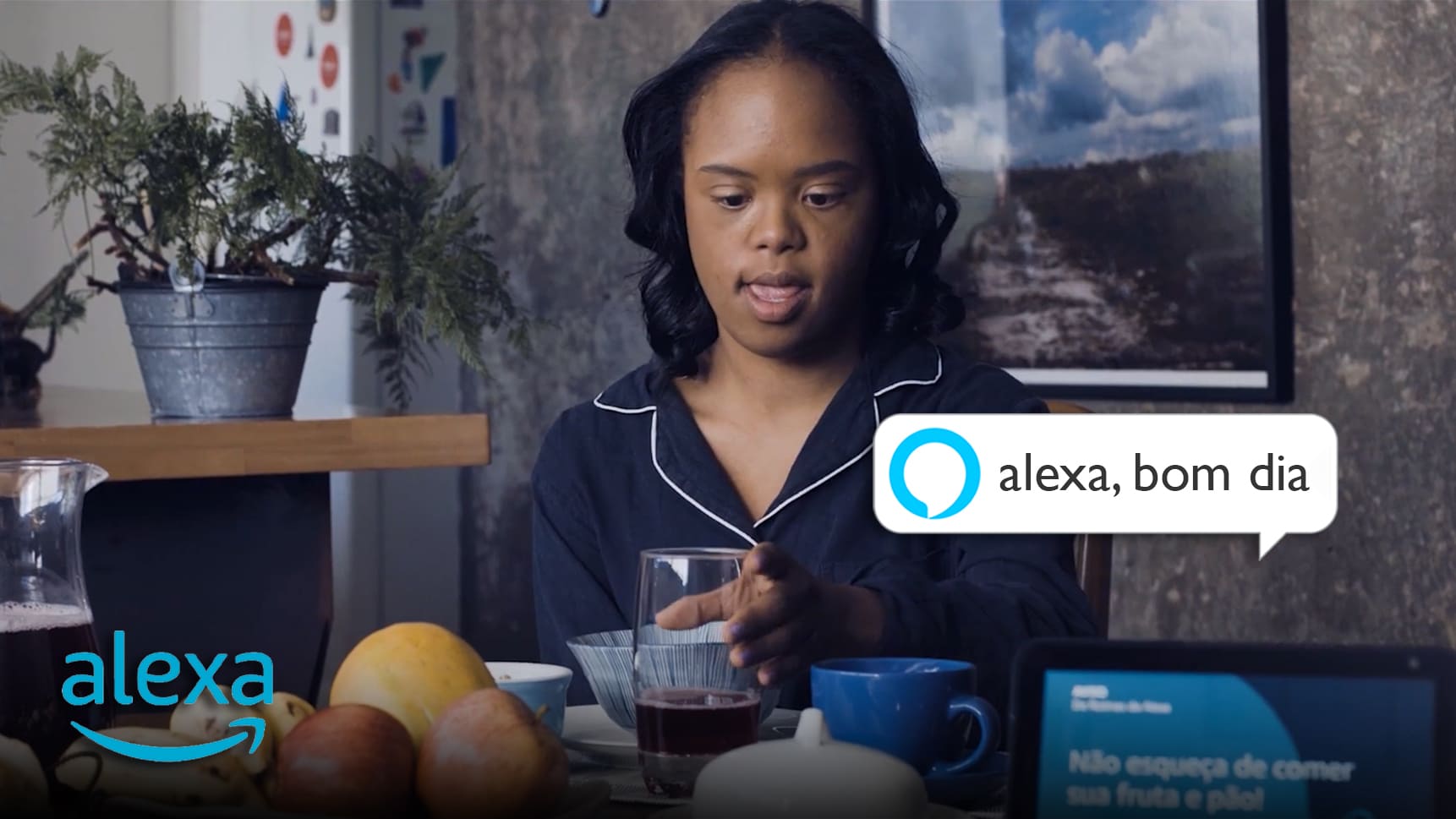 Garota negra com trissomia do cromossomo 21 está sentada à mesa no café da manhã e interagindo com recursos de acessibilidade da Alexa.