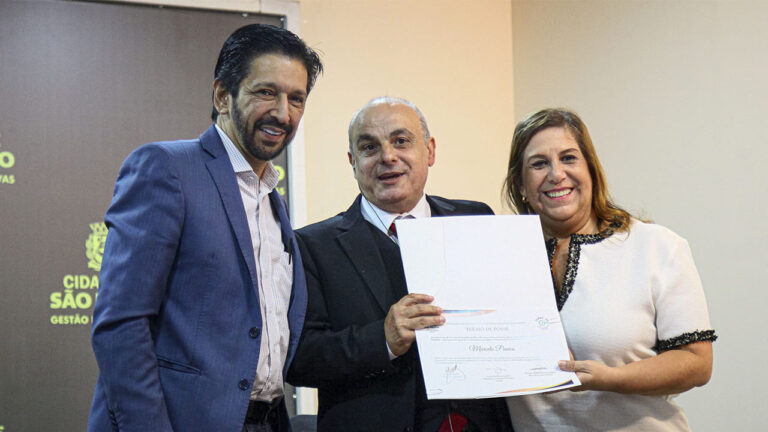 Foto da cerimônia de posse do COMAS, com o prefeito de São Paulo Ricardo Nunes, o advogado cego Marcelo Panico e a Secretária Municipal da Pessoa com Deficiência Silvia Grecco.