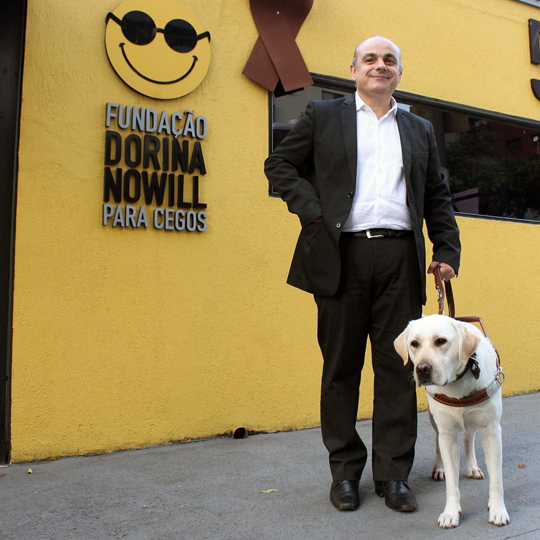 Foto do advogado cego e novo vice-presidente do COMAS, Marcelo Panico e seu cão-guia, a Rudy, em frente a Fundação Dorina Nowill para Cego Cegos.