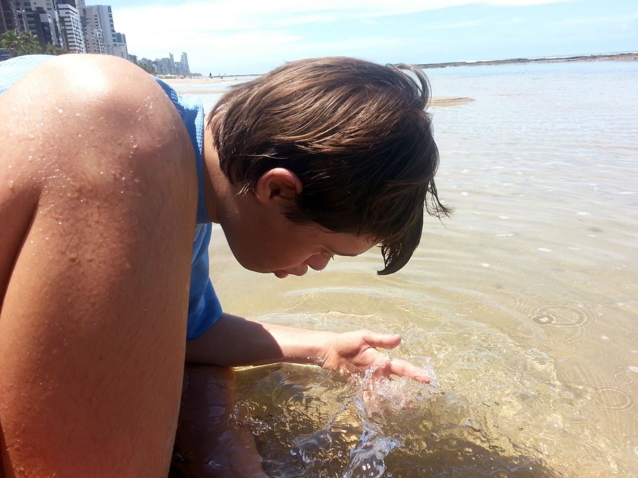 Augusto, que vive o lado b do autismo com síndrome de down, brincando com a água do mar.