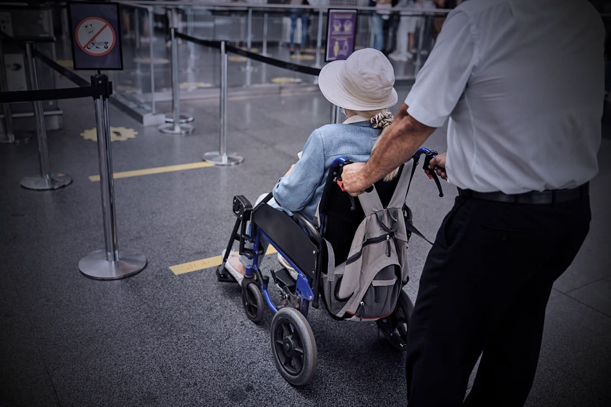 Pessoa idosa em cadeira de rodas recebe assistência em aeroporto.