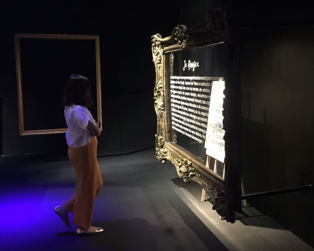 Foto de mulher observando a obra com moldura e textos colados no vidro.