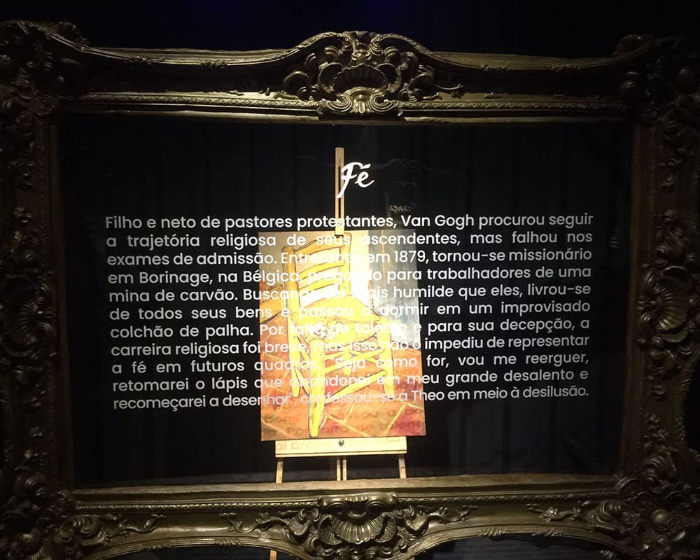 Foto da exposição de Van Gogh Live 8K, mostrando o quadro “A Cadeira” e o texto colado no vidro.