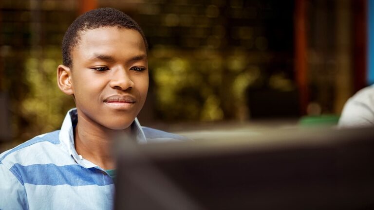 Garoto negro sentado em frente ao computador, pelo programa Portas Abertas de diversidade e qualificação de jovens com e sem deficiência.
