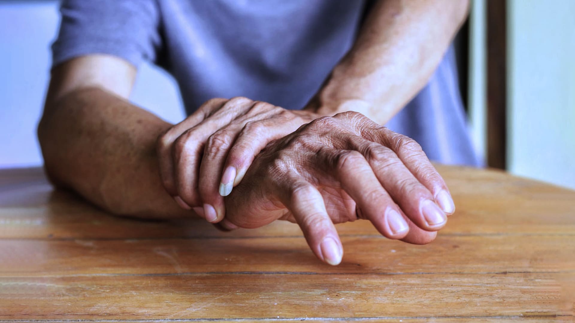 Pessoa estabiliza a mão com tremores segurando firme o próprio punho. Parkinson afeta 10 milhões da população global.