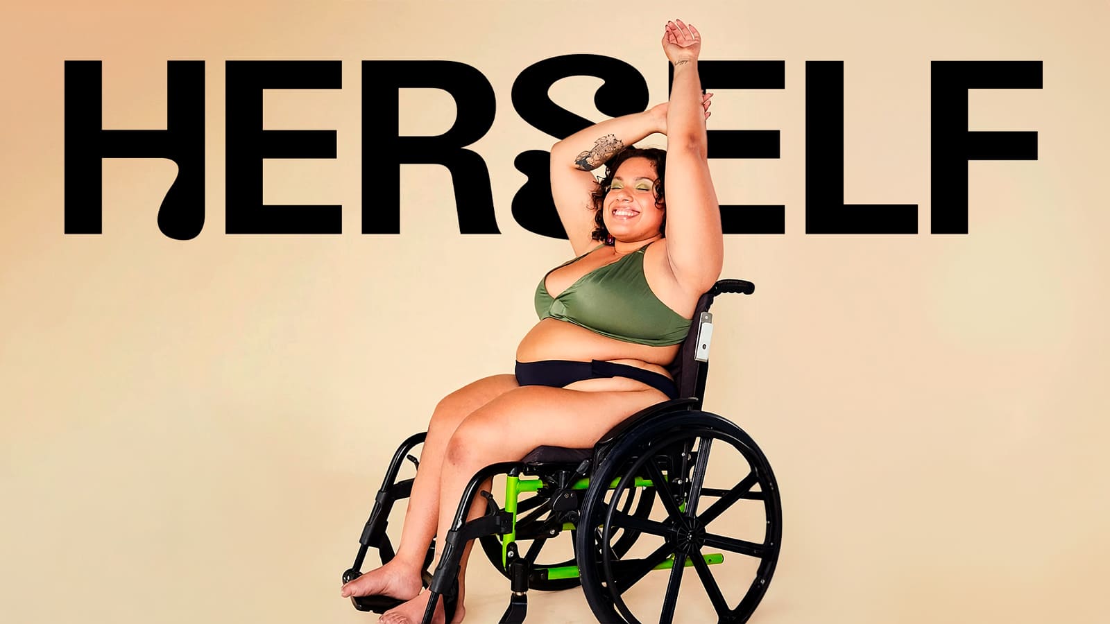 Foto com o nome Herself retrata uma pessoa branca em cadeira de rodas. Ela está sorrindo e com os olhos fechados. Com seu braço direito dobrado acima da cabeça, ela segura o braço esquerdo esticado para o alto. Usa a calcinha absorvente adaptada e top da marca.