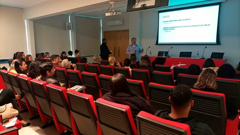 Pessoas estão sentadas assistindo ao workshop no auditório do Sincovaga. À frente, o médico e auditor fiscal José Carlos do Carmo (Kal) está conduzindo a apresentação.